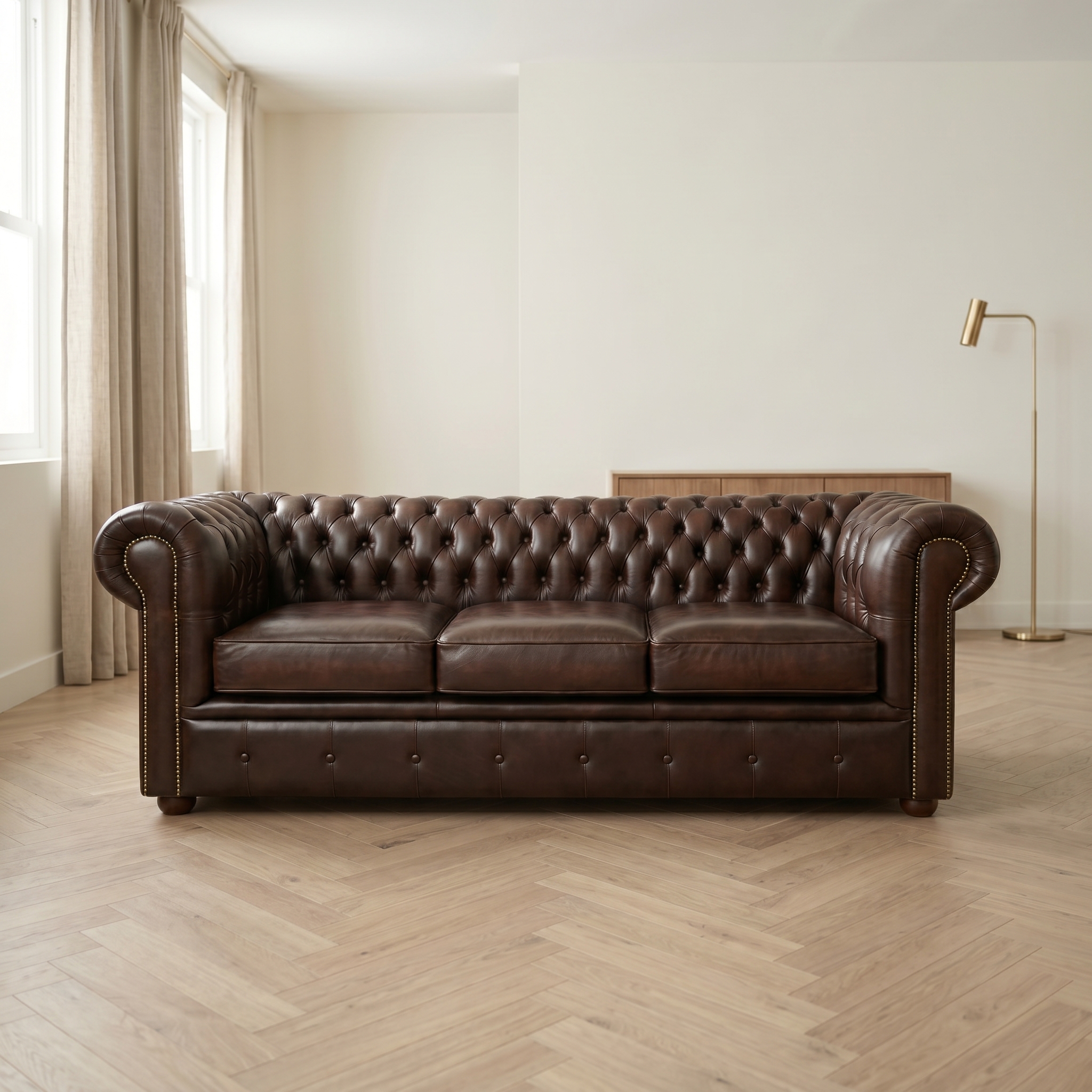A three-seater dark brown leather Newman and Bright sofa in a chesterfield design, positioned in a minimalist room with light herringbone floors, neutral beige curtains, and a gold floor lamp.